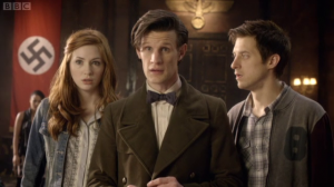 The Doctor, flanked by Amy and Rory, stands in front of a swastika flag